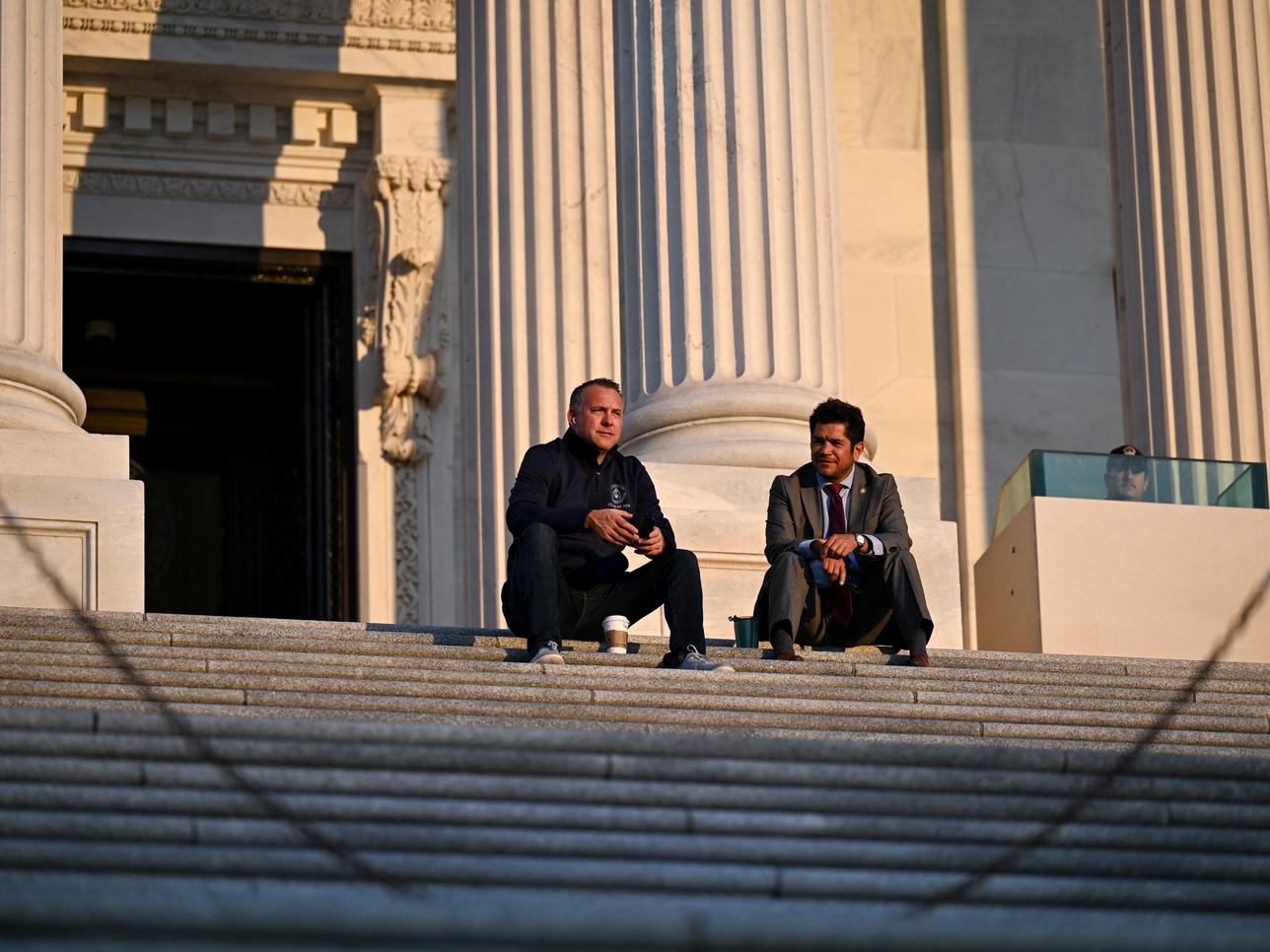 Two members of Congress sit on the steps during overnight debate on the bill.