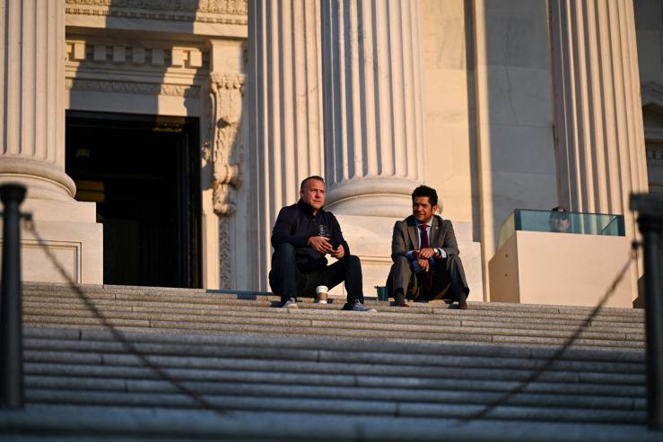 Two members of Congress sit on the steps during overnight debate on the bill.