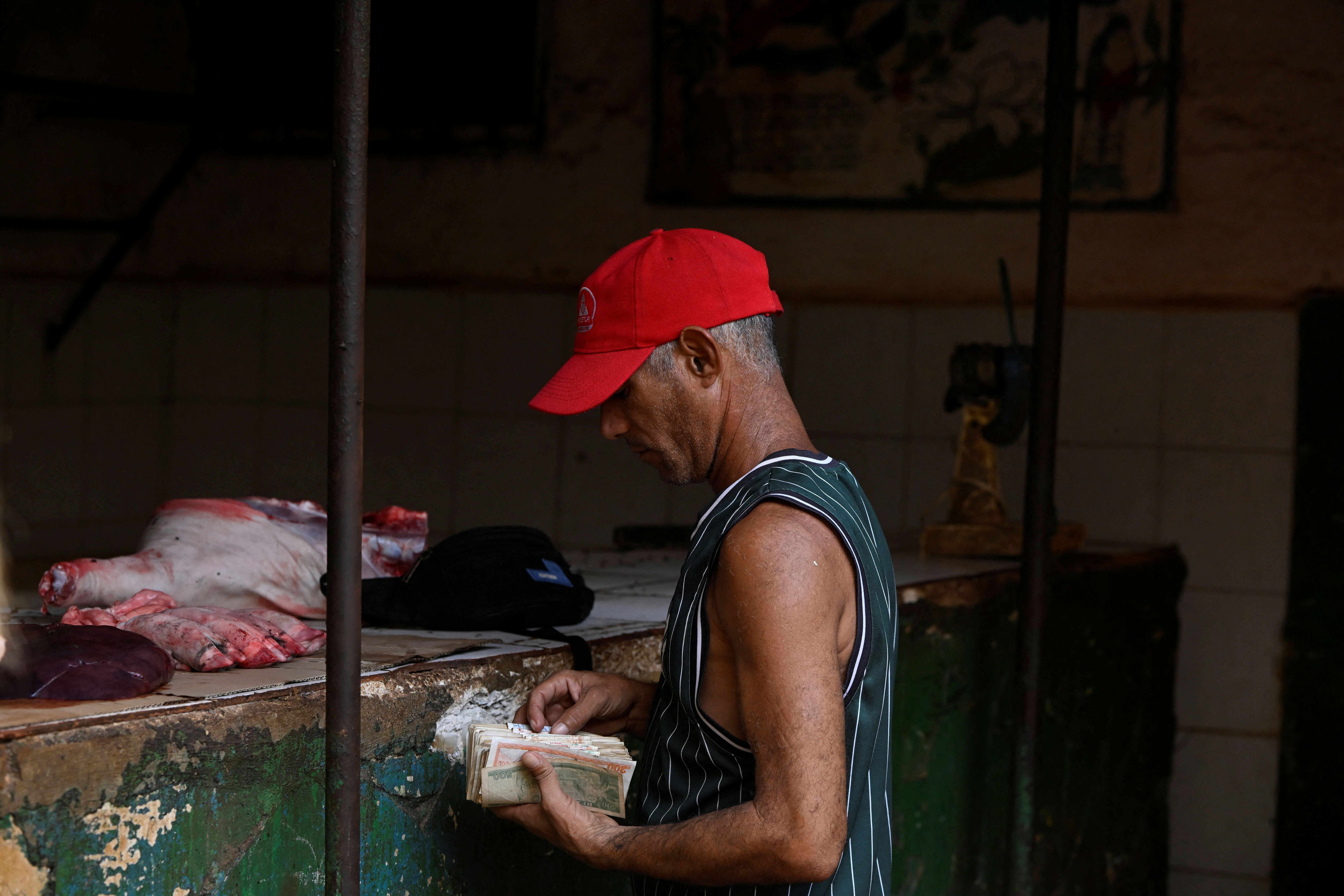 A man counts Cuban pesos before buying pork at a food market.