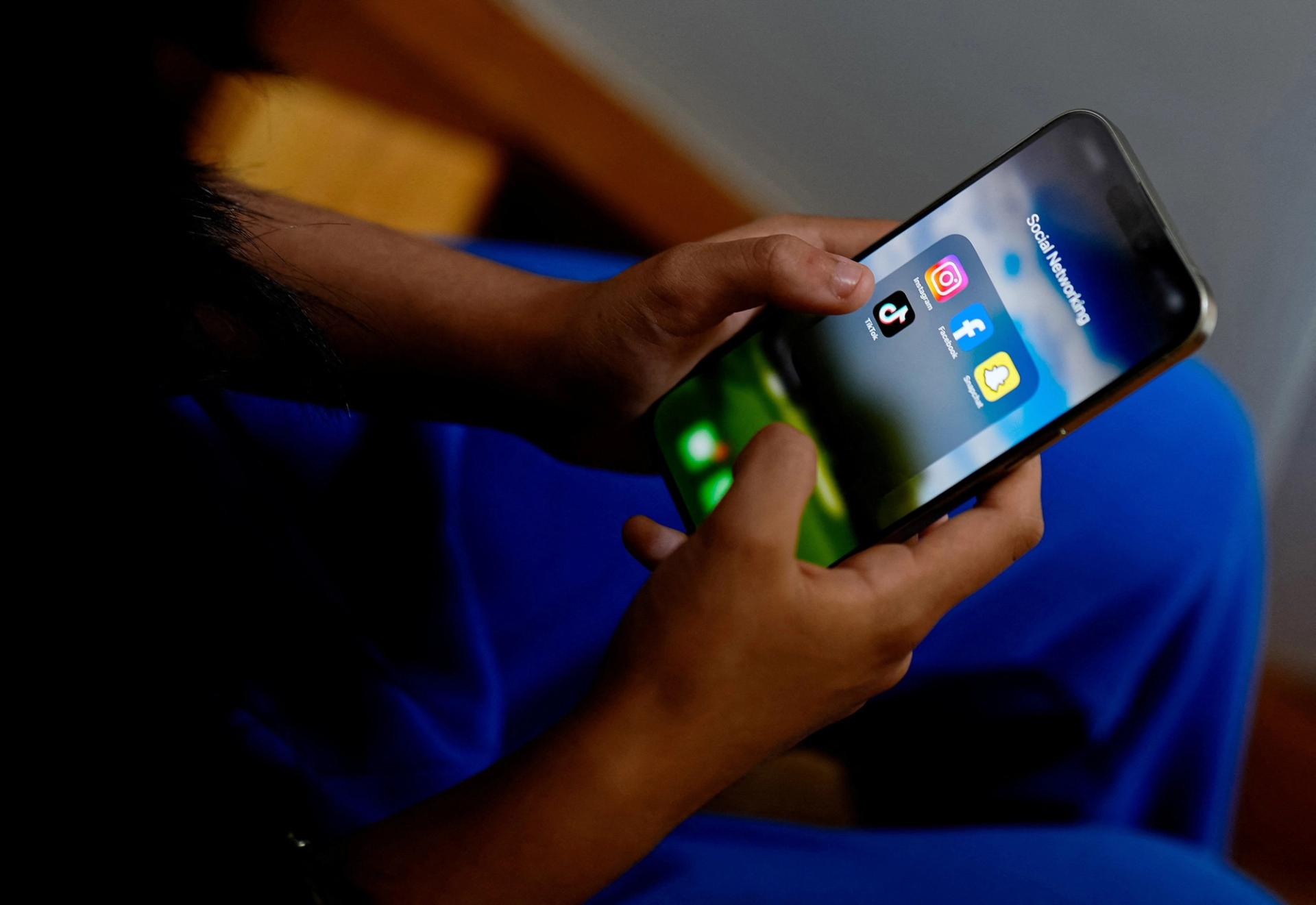 A high school student poses with her mobile phone, which shows social media applications