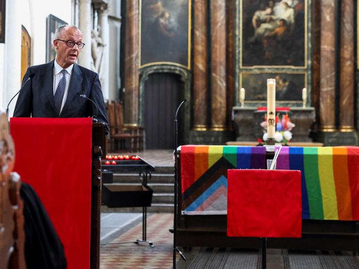 German Chancellor Friedrich Merz speaks next to an altar draped in rainbow flags during a memorial service