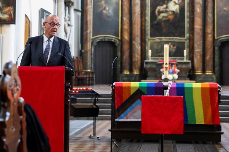 German Chancellor Friedrich Merz speaks next to an altar draped in rainbow flags during a memorial service
