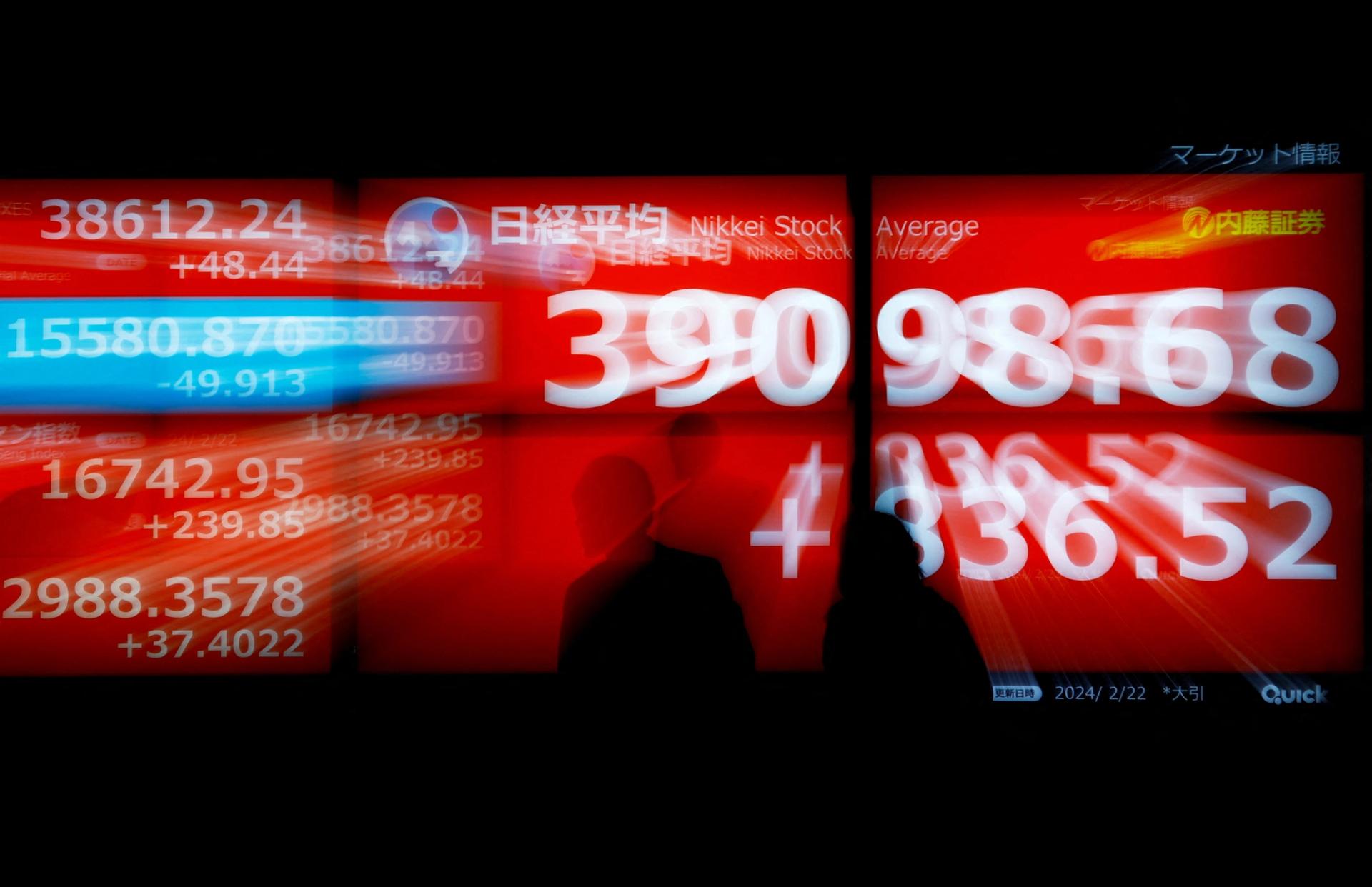Passersby look at electric screens, displying Japan's Nikkei share average which surged to a record high, outside of a brokerage in Tokyo, Japan February 22, 2024. REUTERS/Issei Kato