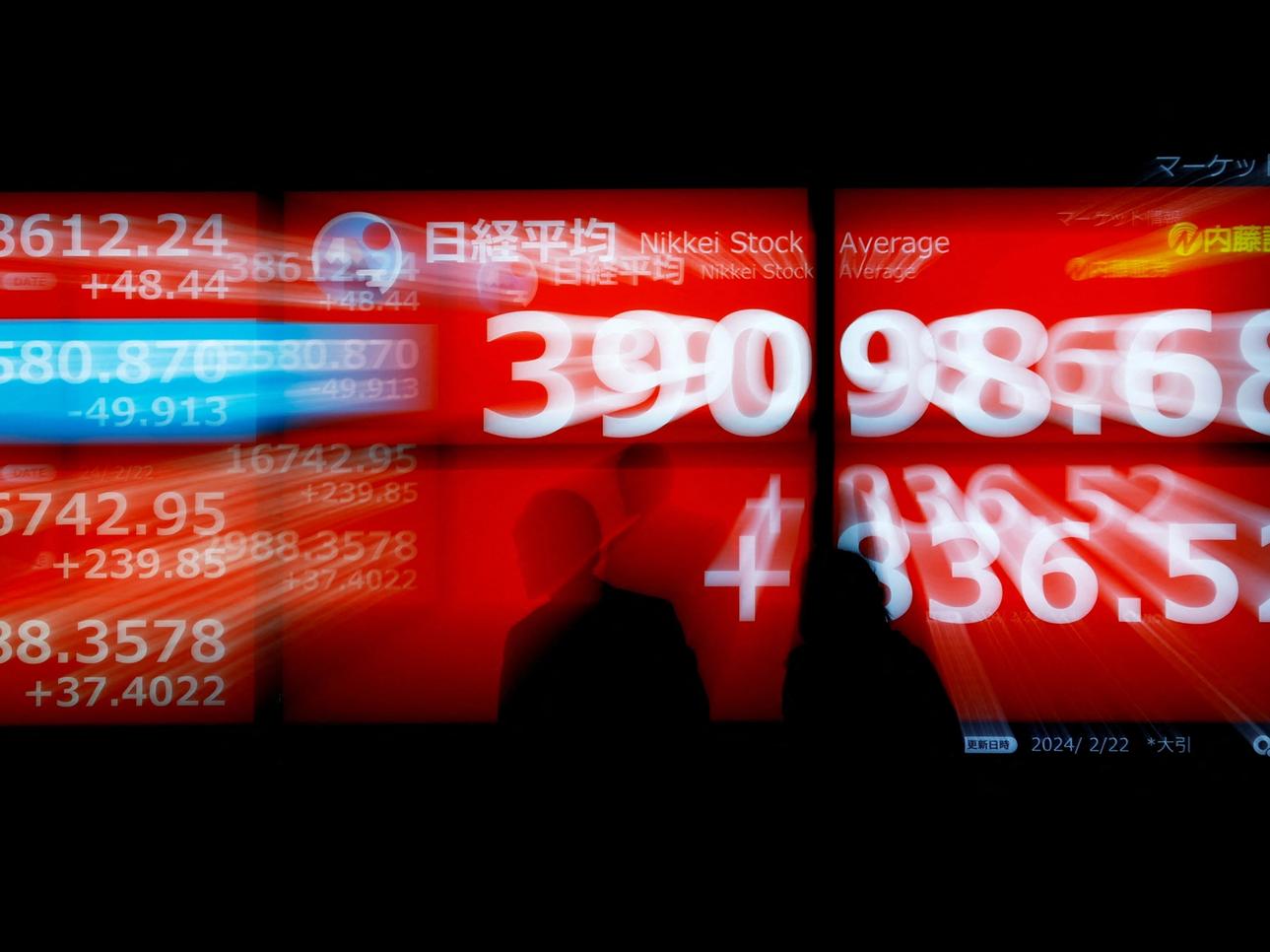 Passersby look at electric screens, displying Japan's Nikkei share average which surged to a record high, outside of a brokerage in Tokyo, Japan February 22, 2024. REUTERS/Issei Kato