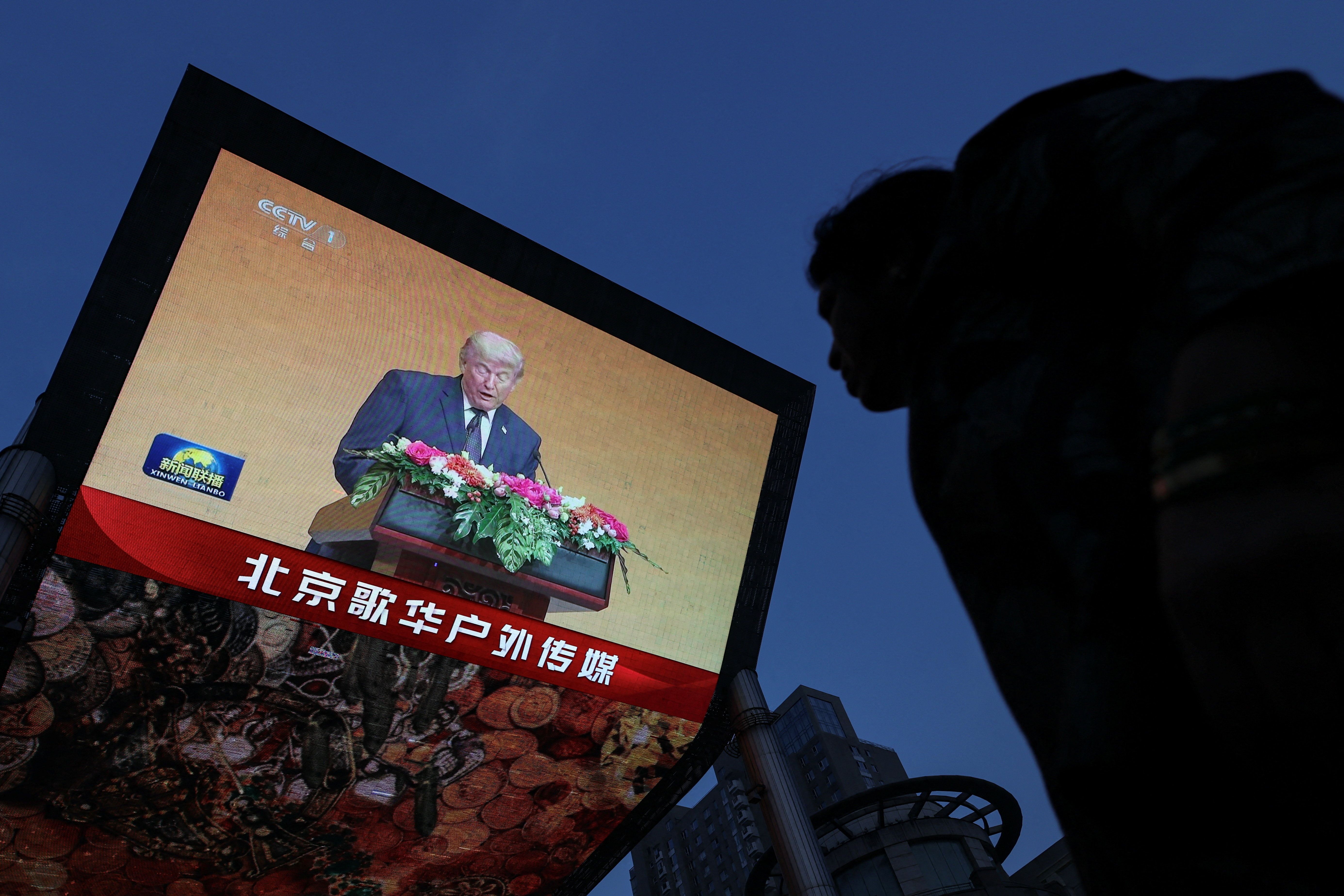 A person looks on near a giant screen showing news footage of U.S. President Donald Trump attending a welcoming banquet held by Chinese President Xi Jinping at the Great Hall of the People, in Beijing