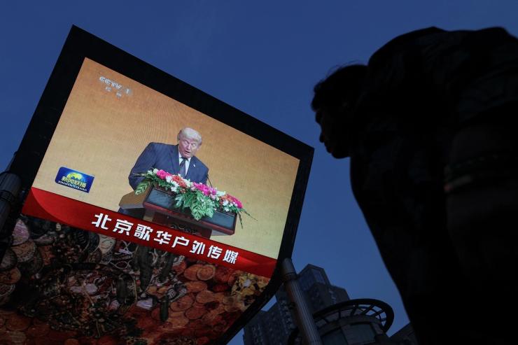 A person looks on near a giant screen showing news footage of U.S. President Donald Trump attending a welcoming banquet held by Chinese President Xi Jinping at the Great Hall of the People, in Beijing