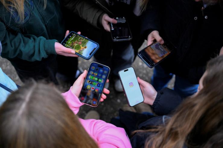 Teenagers pose for a picture while looking at their phones