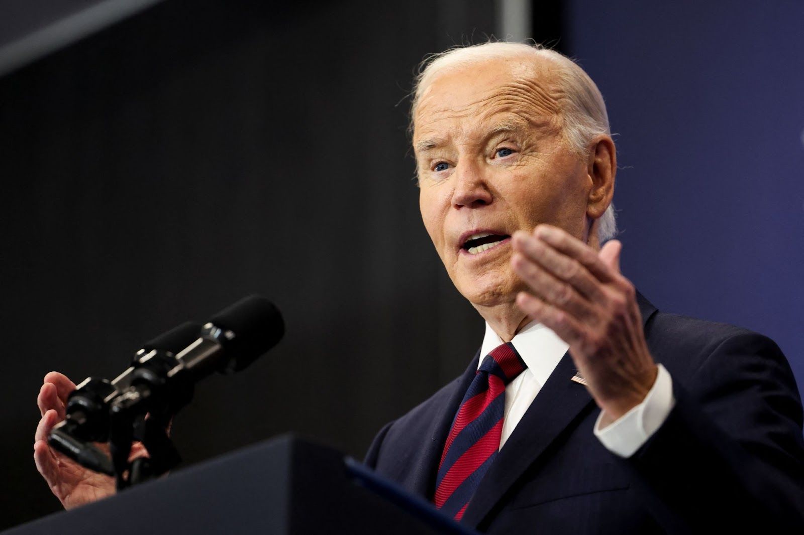 Joe Biden, wearing a dark suit and striped tie, gives a speech on stage