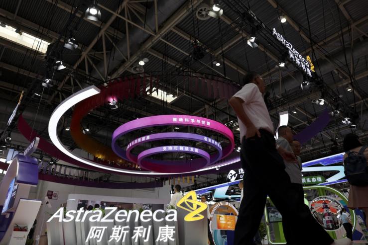 People walk past the AstraZeneca booth during the China International Supply Chain Expo in Beijing