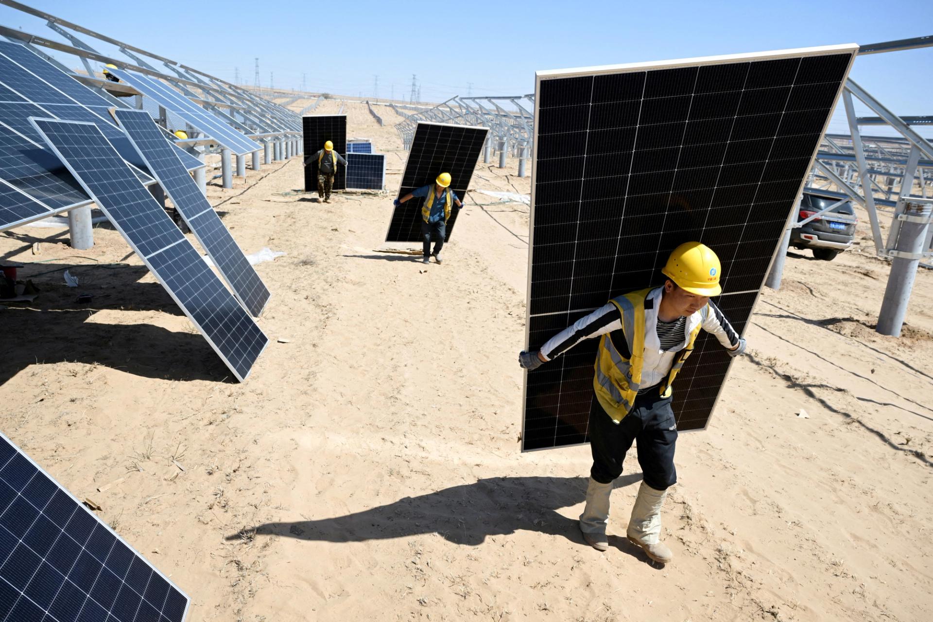 Workers carry solar panels to install them at a solar farm in the desert, in Lingwu, Ningxia Hui Autonomous Region, China.