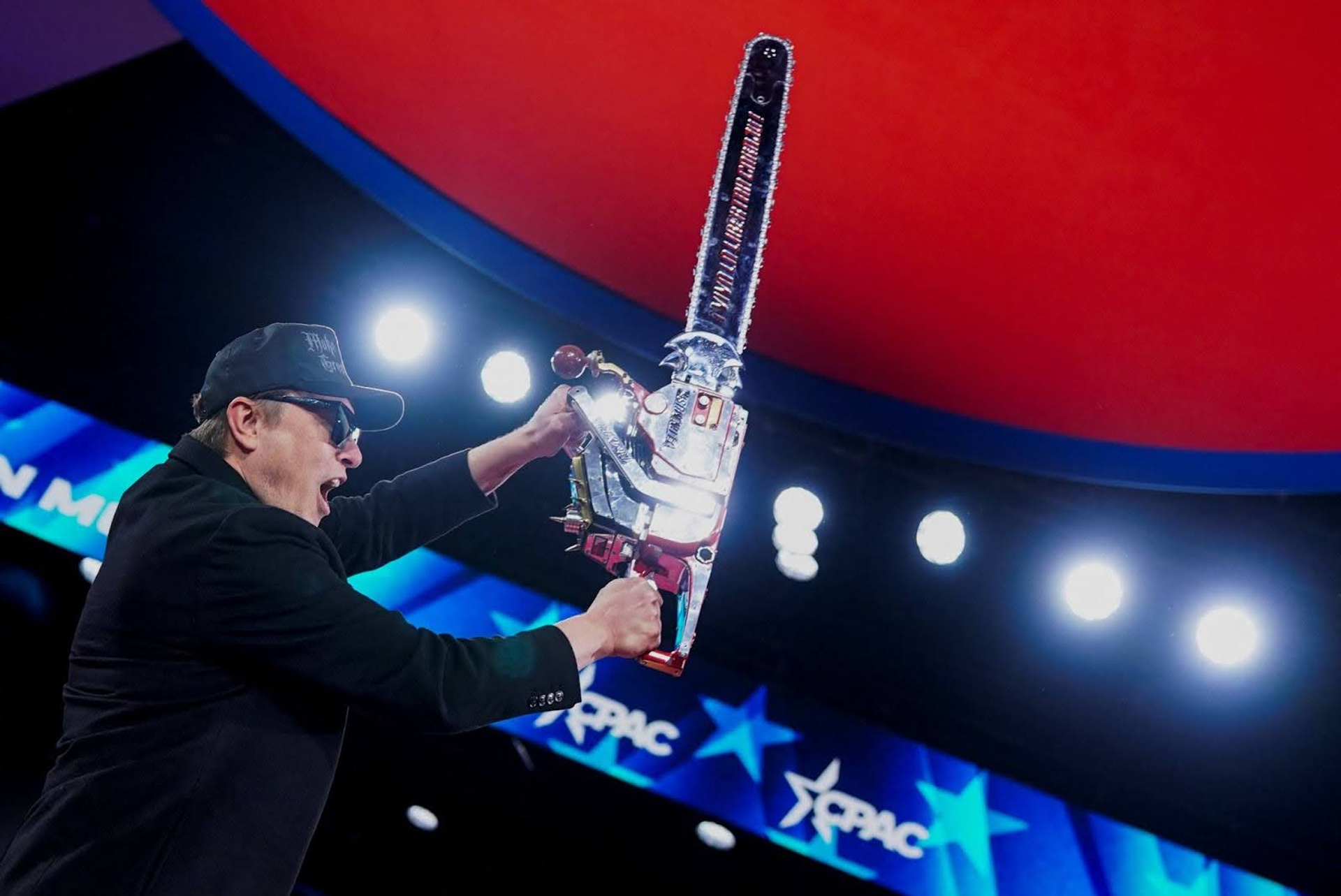 Elon Musk holding a chainsaw. 