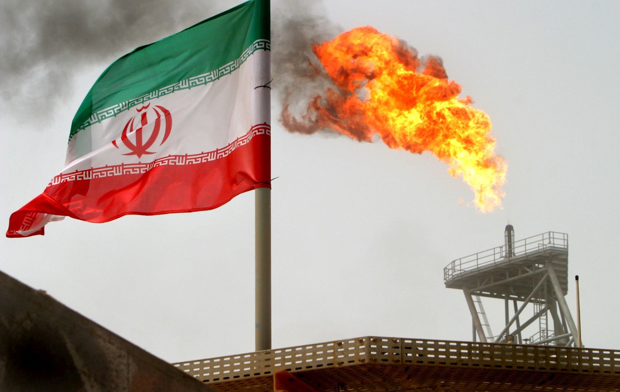 A gas flare on an oil production platform is seen alongside an Iranian flag.