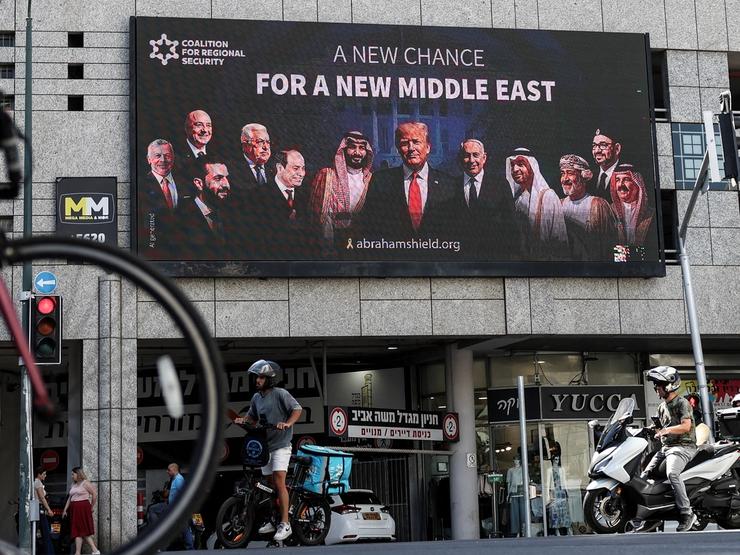 People walk by a billboard calling for the expansion of the Abraham Accords