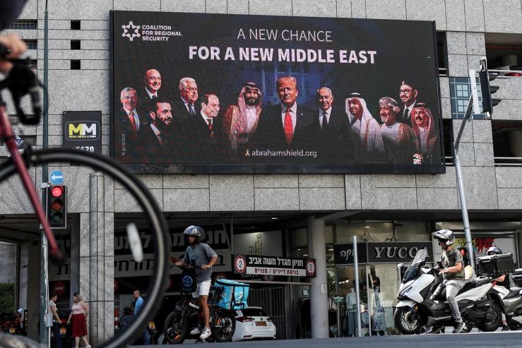 People walk by a billboard calling for the expansion of the Abraham Accords