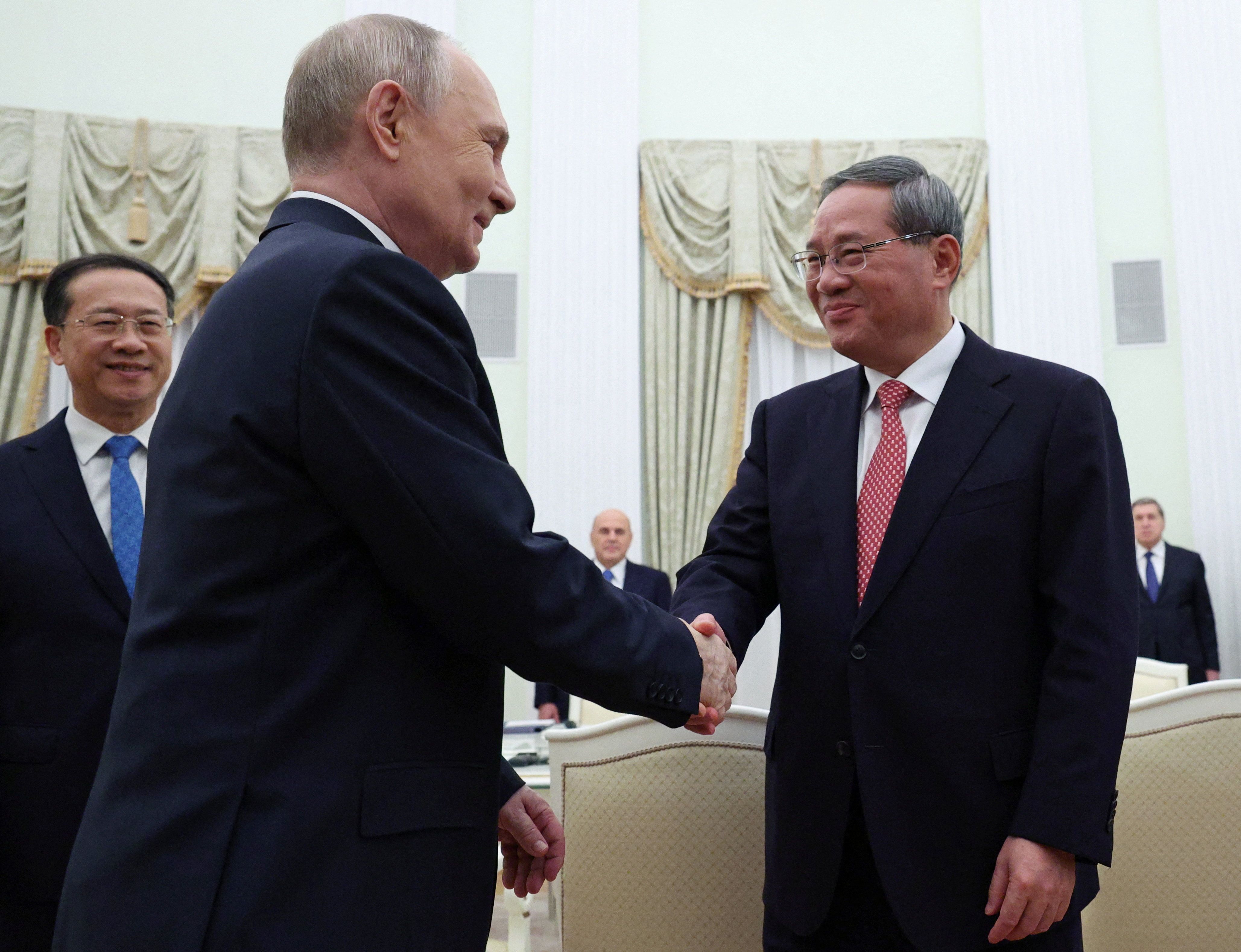 Russian President Vladimir Putin shakes hands with Chinese Premier Li Qiang.