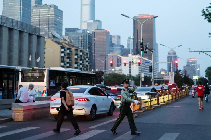 A paramilitary police officer crosses the street, with Beijing Central Business District skyline seen in the background