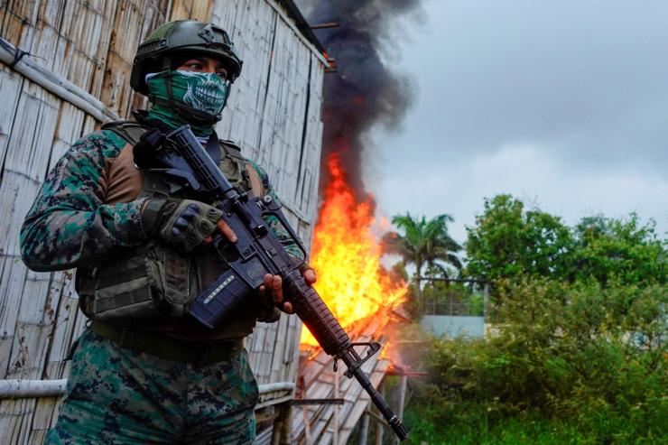 A soldier stands guard next to a house set on fire by police in a search operation in Ecuador.