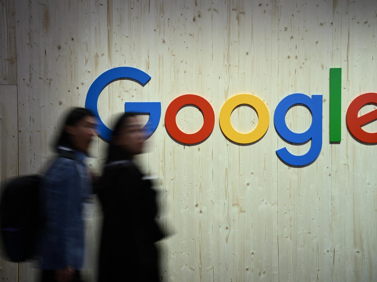 People walk next to a Google logo.