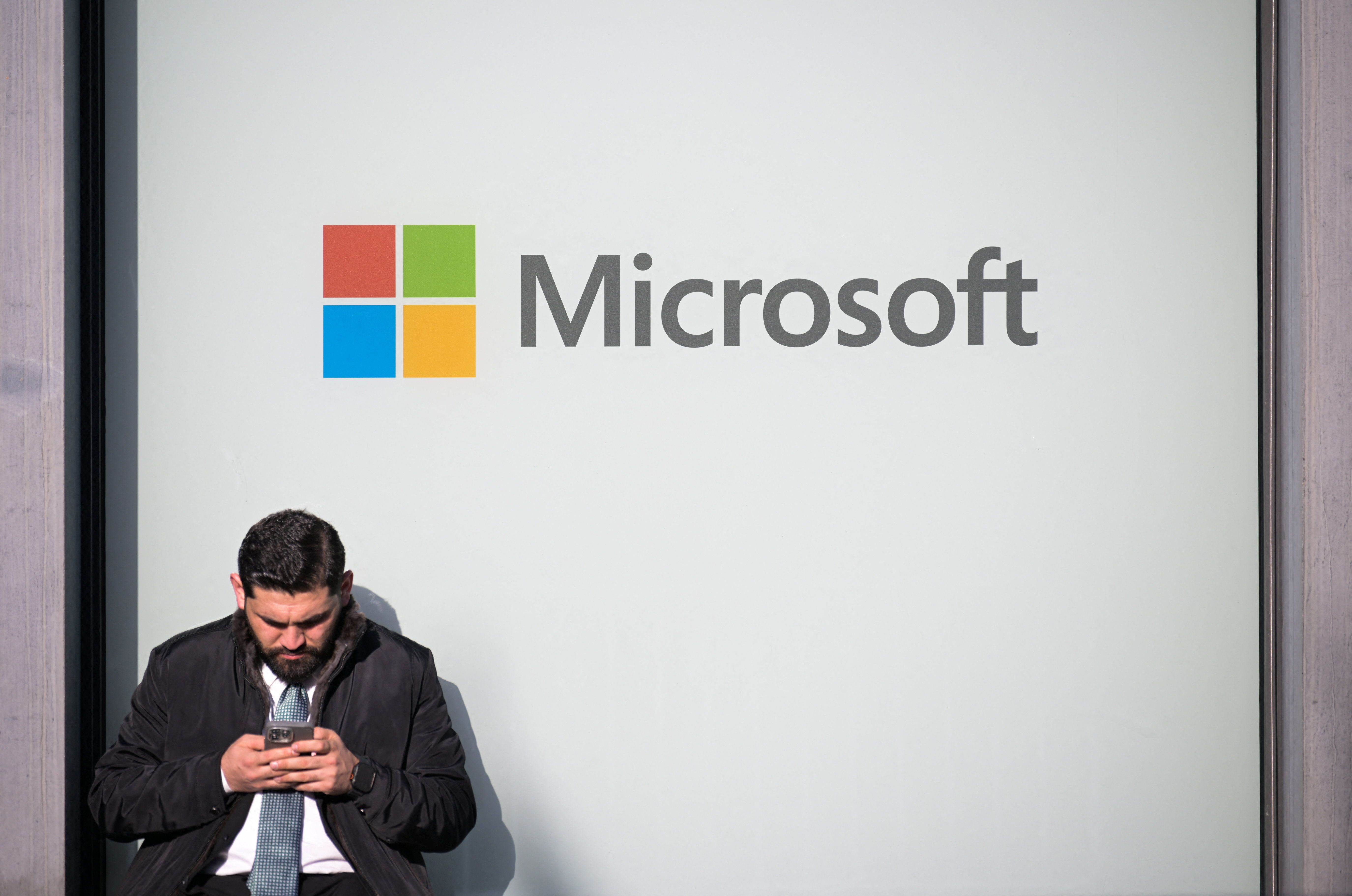 A man uses a phone next to a Microsoft logo 
