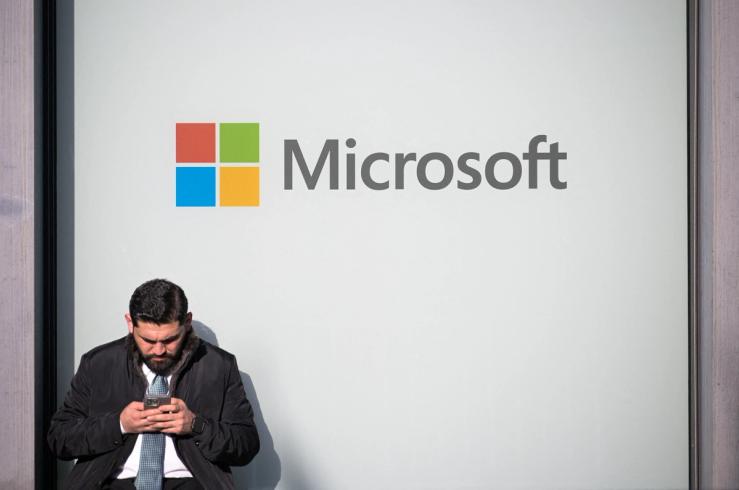 A man uses a phone next to a Microsoft logo