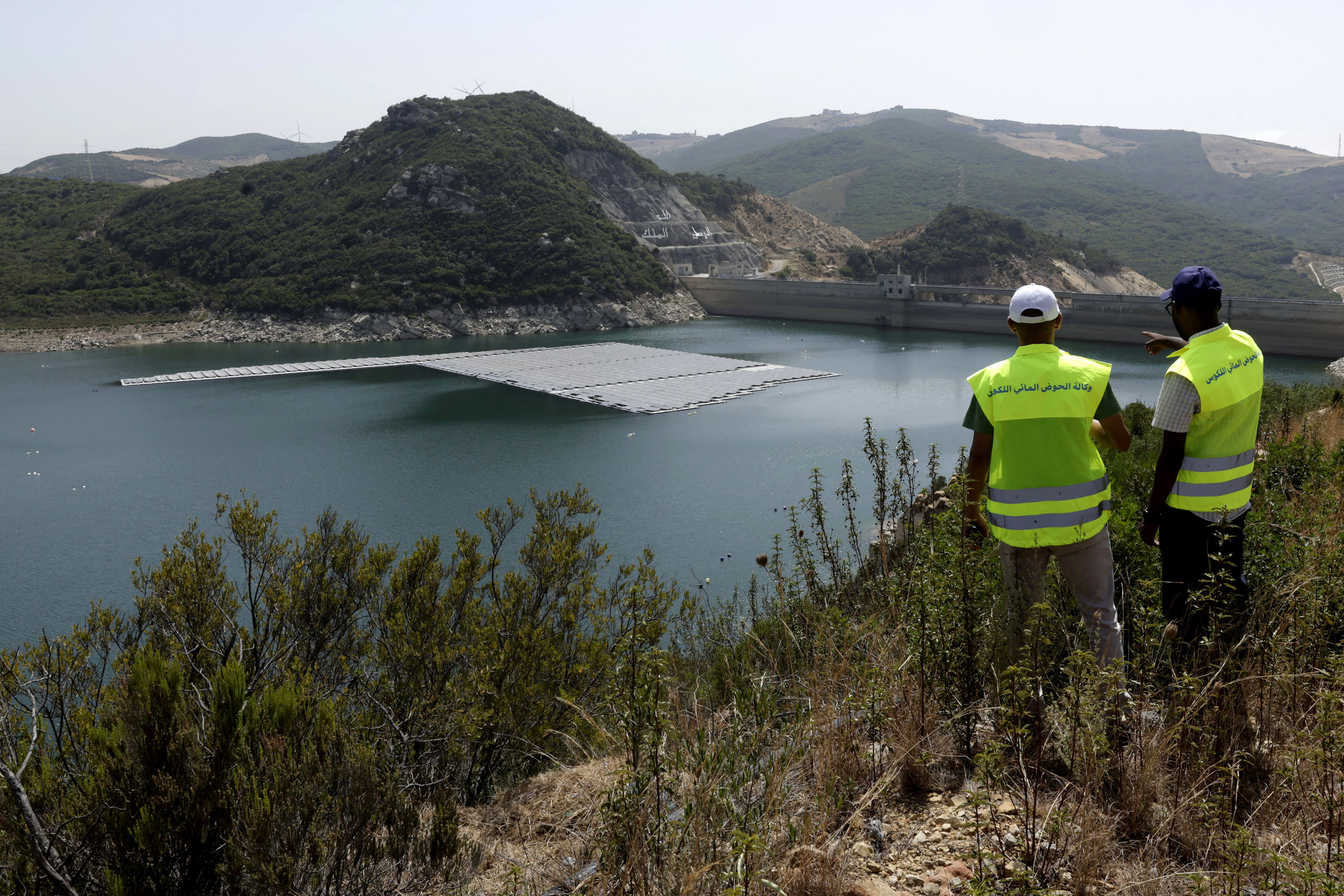 Workers watch from a hill a floating photovoltaic solar installation on the Oued Rmel dam.