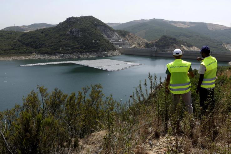 Workers watch from a hill a floating photovoltaic solar installation on the Oued Rmel dam.