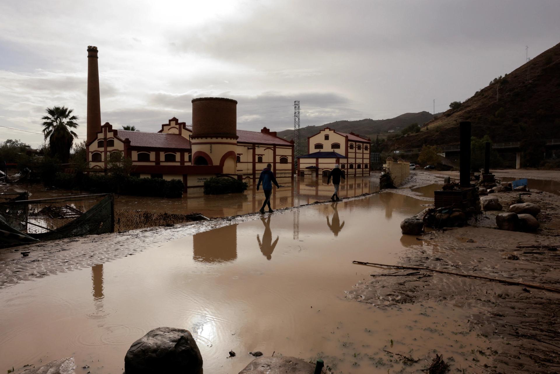 Men walk along a flooded area after heavy rains and floods in Alora, Spain.