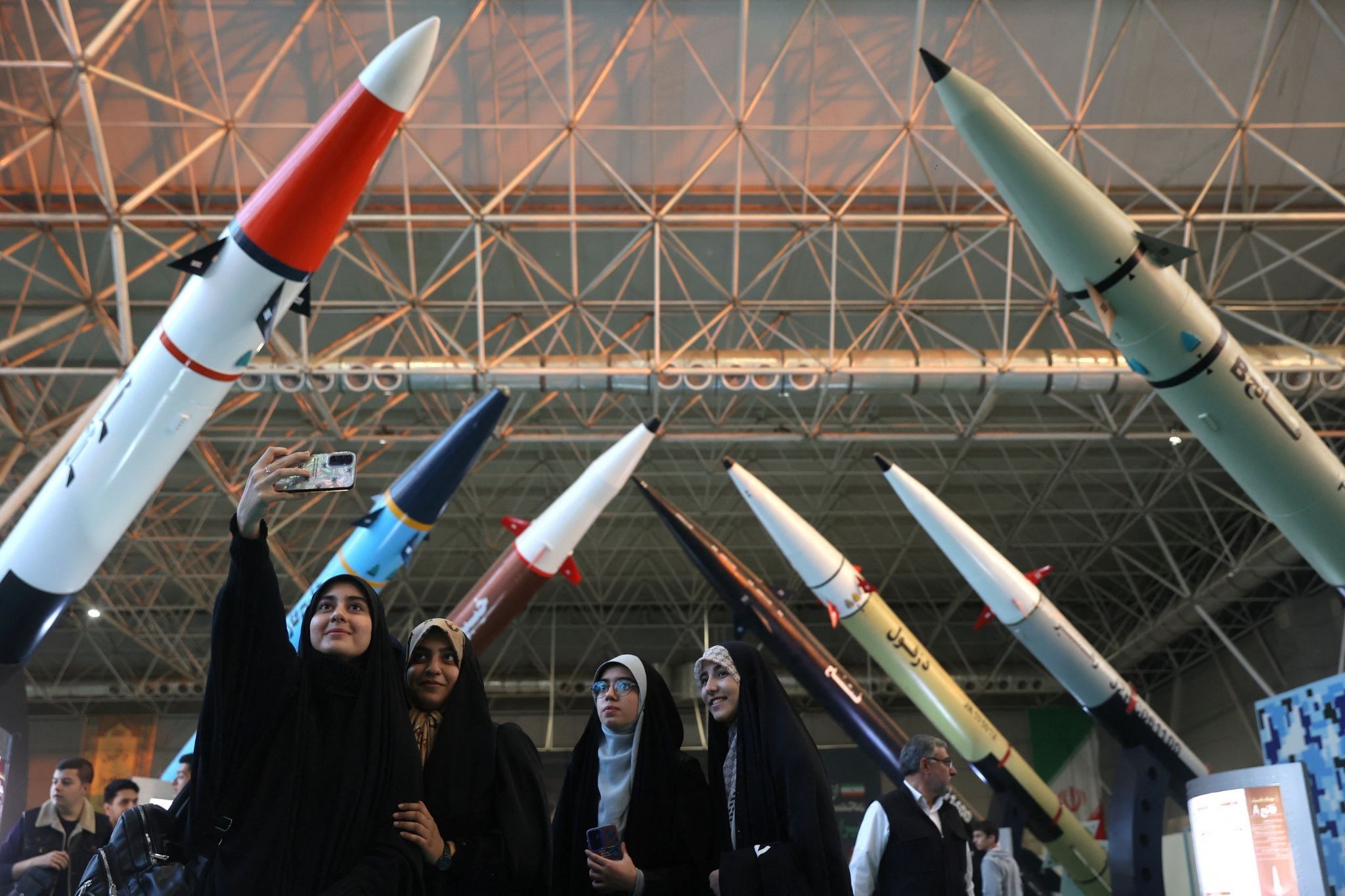 Young Iranian women pose for a selfie in front of a missile display