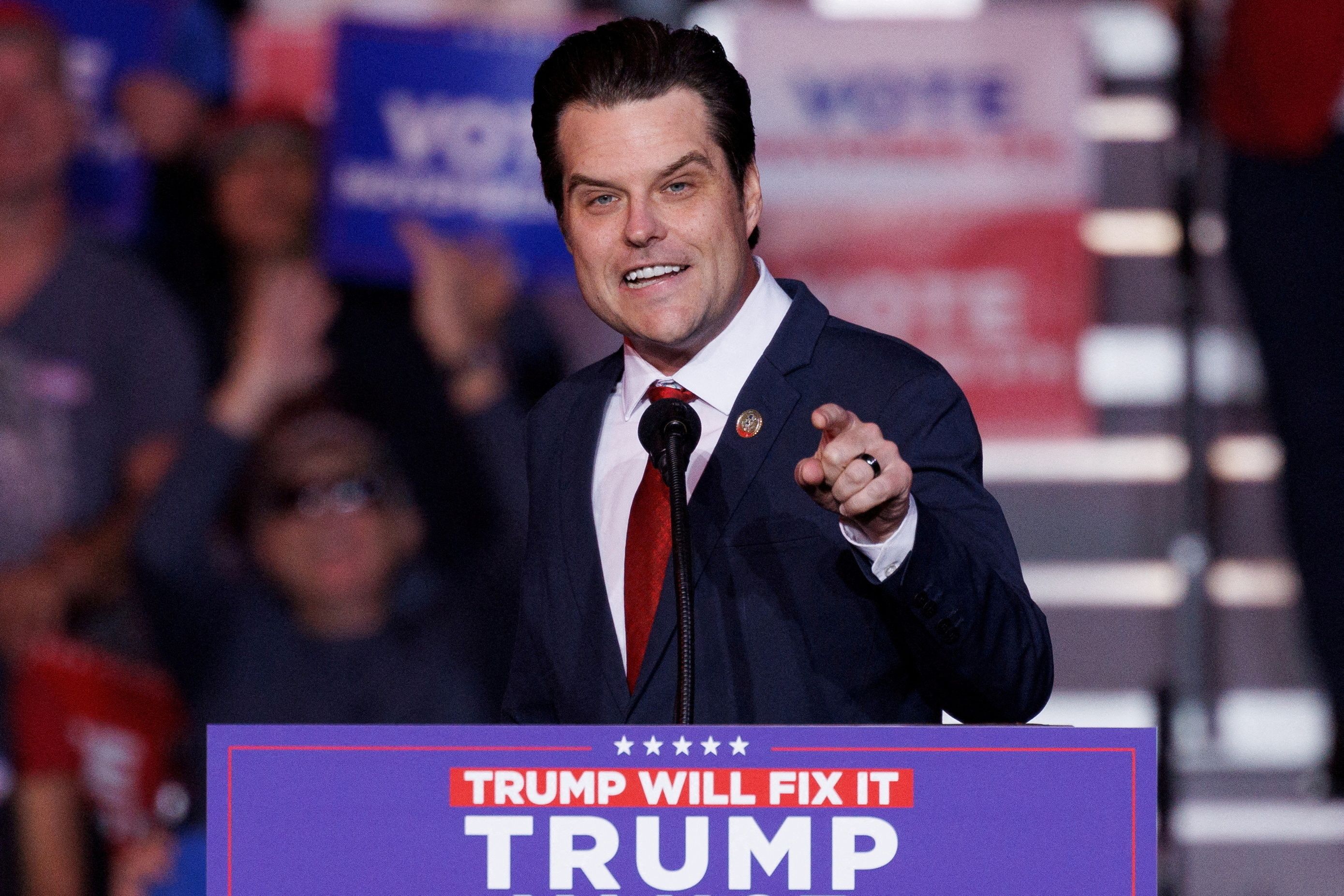 Matt Gaetz, wearing a dark suit and red tie, on stage at a Trump rally.