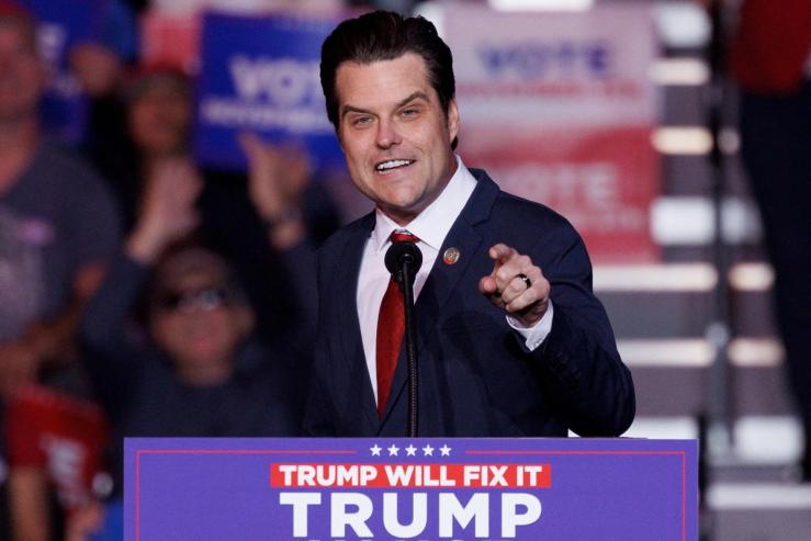 Matt Gaetz, wearing a dark suit and red tie, on stage at a Trump rally.