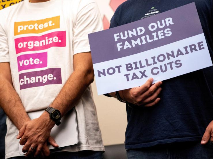 A person with a sign protesting “billionaire tax cuts”