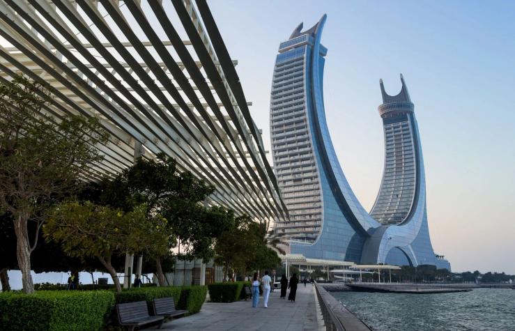 People walk along the waterfront promenade with the Lusail Towers in the background at Lusail City in Doha