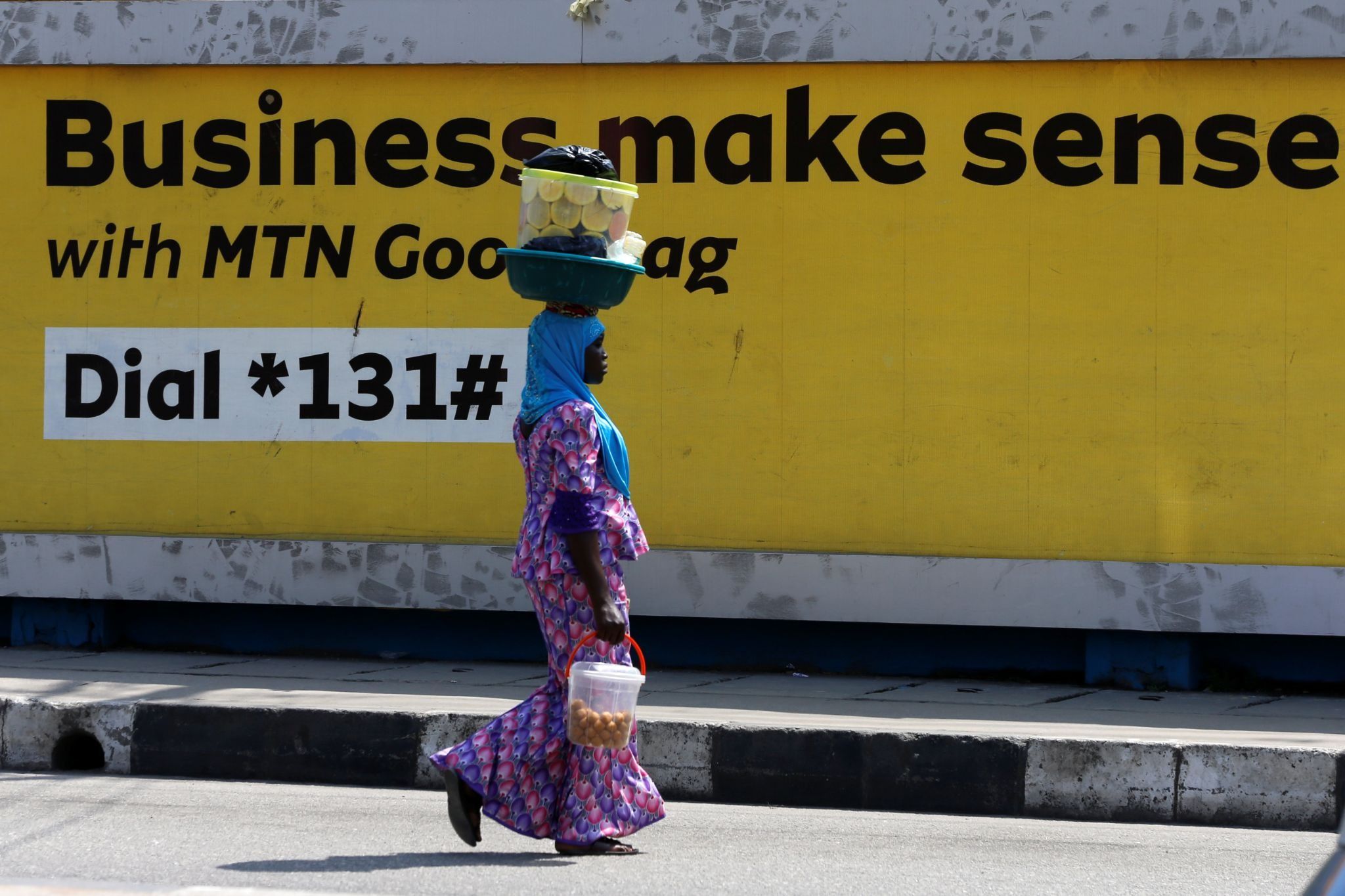 A woman walks past an advertising poster for MTN telecommunication company along a street in Lagos.