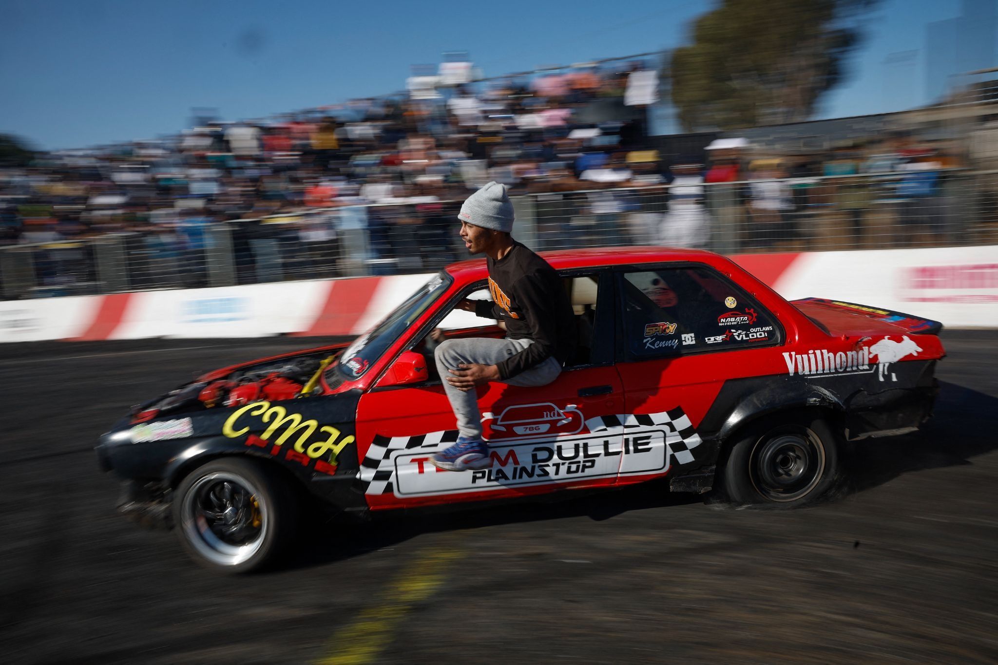 A member of “Team Dullie” hangs out of their car as they drift during a round of spinning at Wheelz n Smoke Arena.