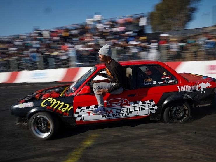 A member of “Team Dullie” hangs out of their car as they drift during a round of spinning at Wheelz n Smoke Arena.