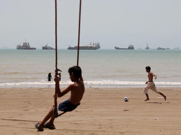 A child plays at the beach, with vessels in the Strait of Hormuz visible near the beach of Bandar Abbas