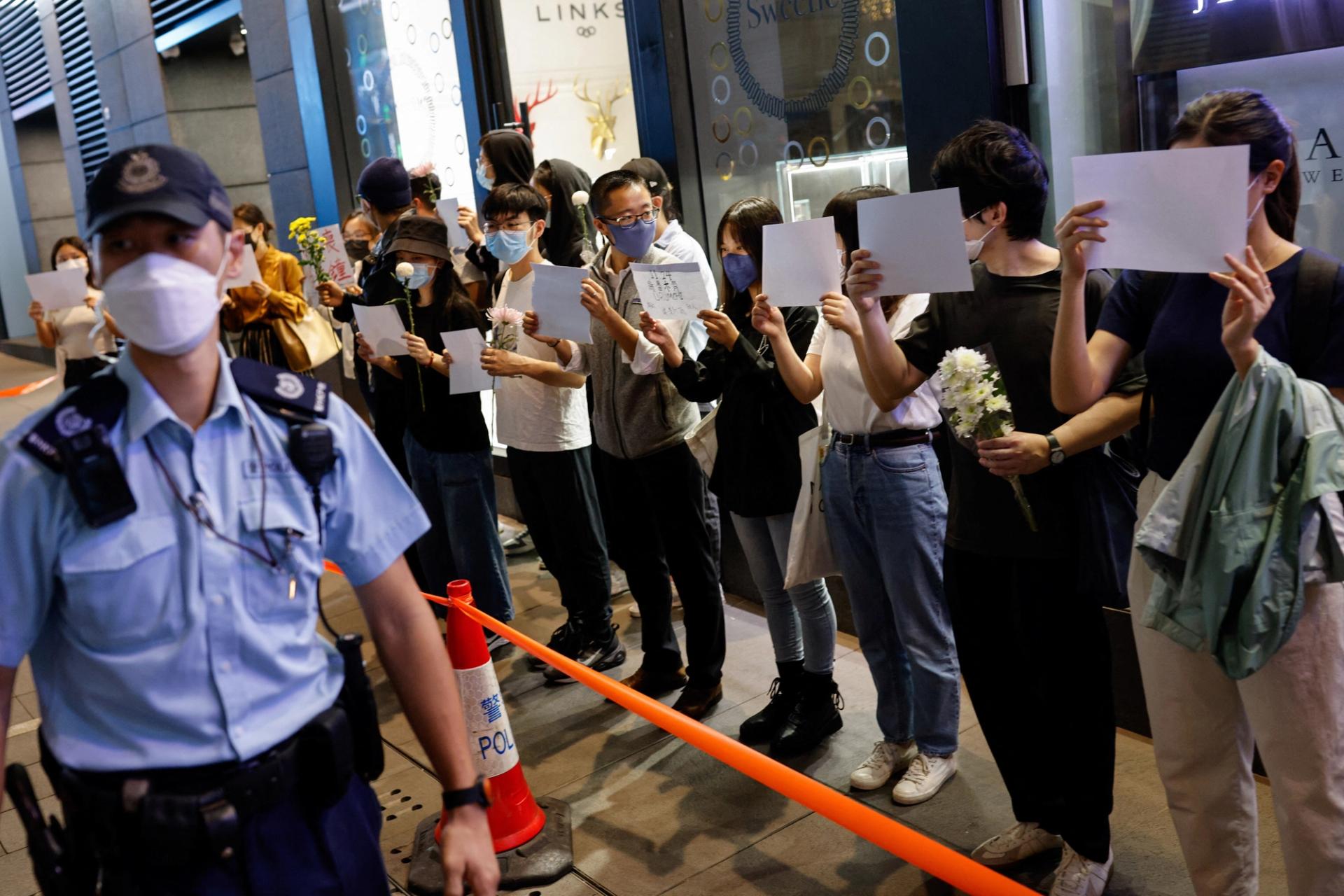People hold white sheets of paper and flowers at a protest in Hong Kong.