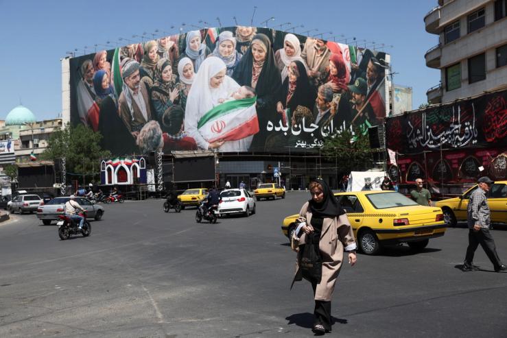 People walk past a billboard with a picture of Iranian people, in Tehran