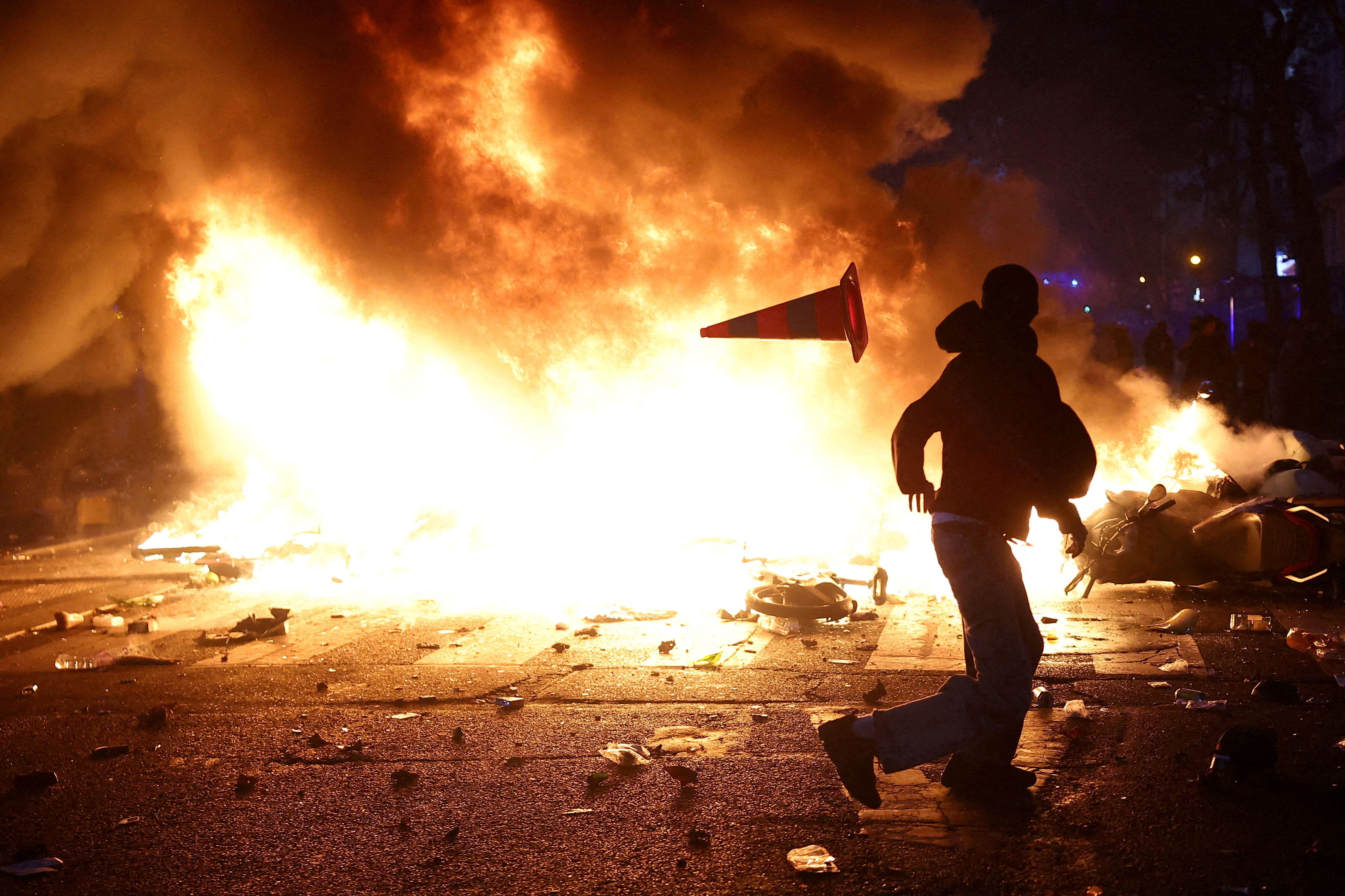 A man throws a plastic traffic cone through a burning barricade amid clashes during a day of demonstrations against the cost of living and rising fuel prices in Paris as part of nationwide protests called by the “Yellow Vests” movement.