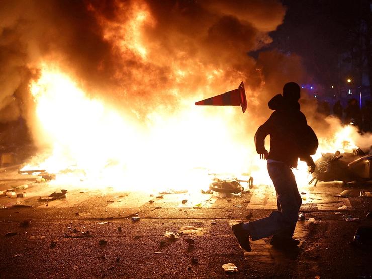 A man throws a plastic traffic cone through a burning barricade amid clashes during a day of demonstrations against the cost of living and rising fuel prices in Paris as part of nationwide protests called by the “Yellow Vests” movement.