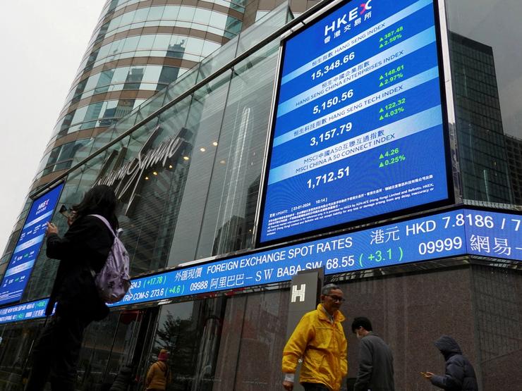 People walk past screens displaying the Hang Seng stock index and stock prices outside the Exchange Square in Hong Kong.