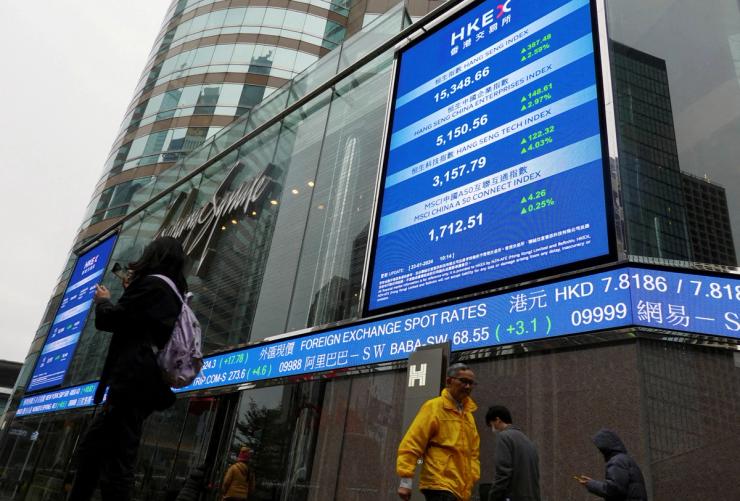 People walk past screens displaying the Hang Seng stock index and stock prices outside the Exchange Square in Hong Kong.