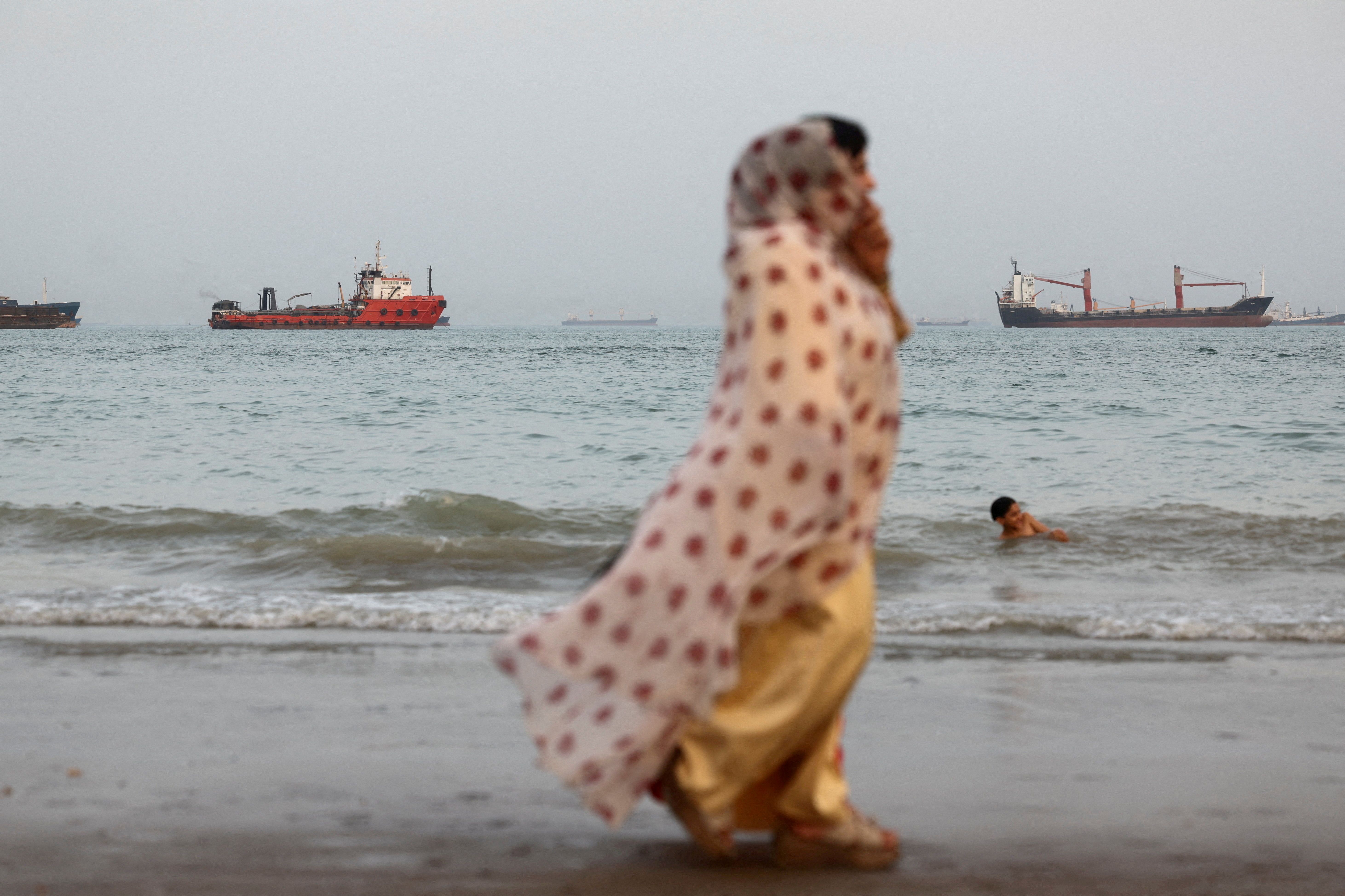 People walk on the beach, with vessels in the Strait of Hormuz visible near the beach of Bandar Abbas, Iran, May 22, 2026