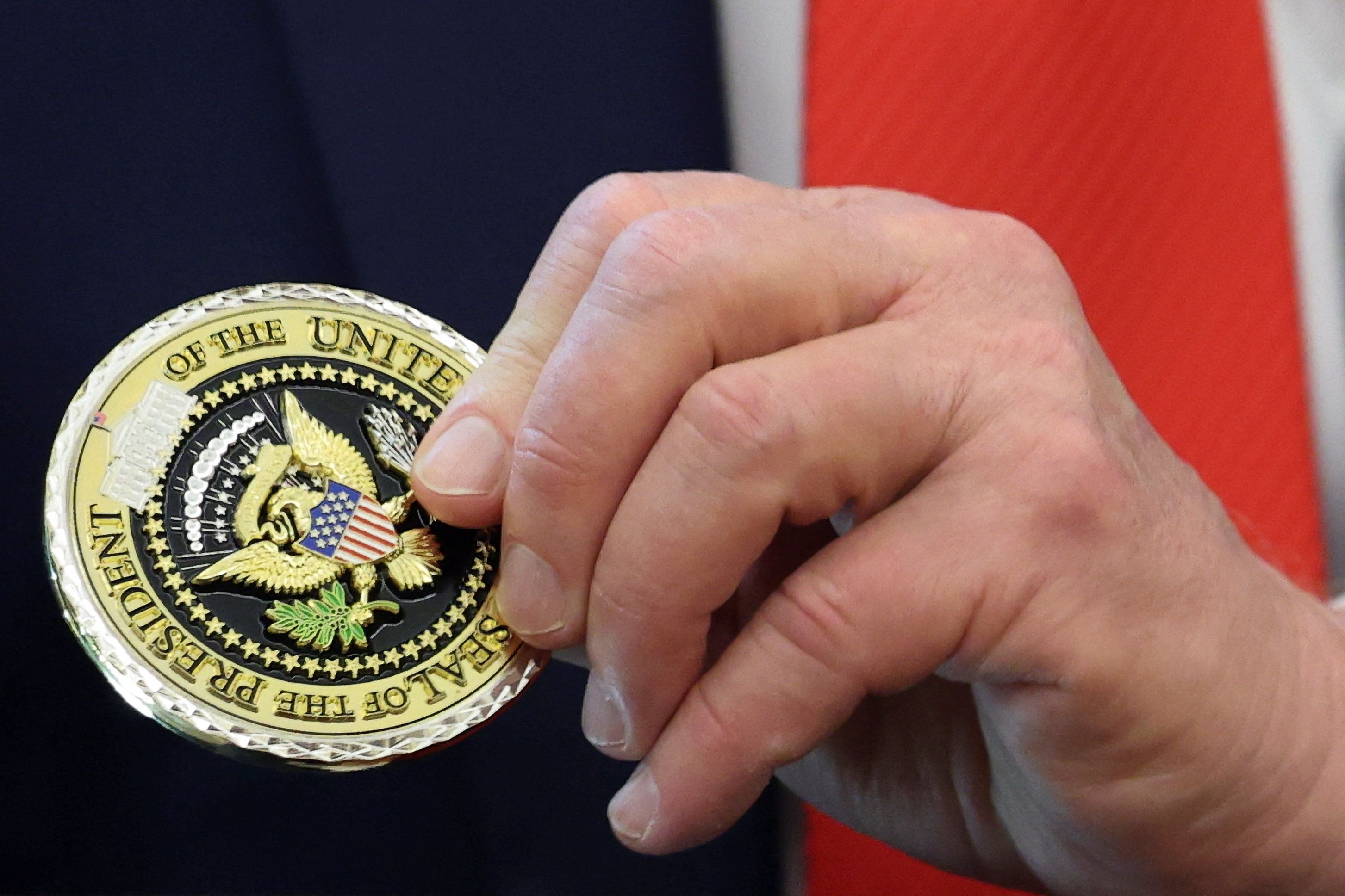 Trump’s hand holding a medal with the presidential seal 