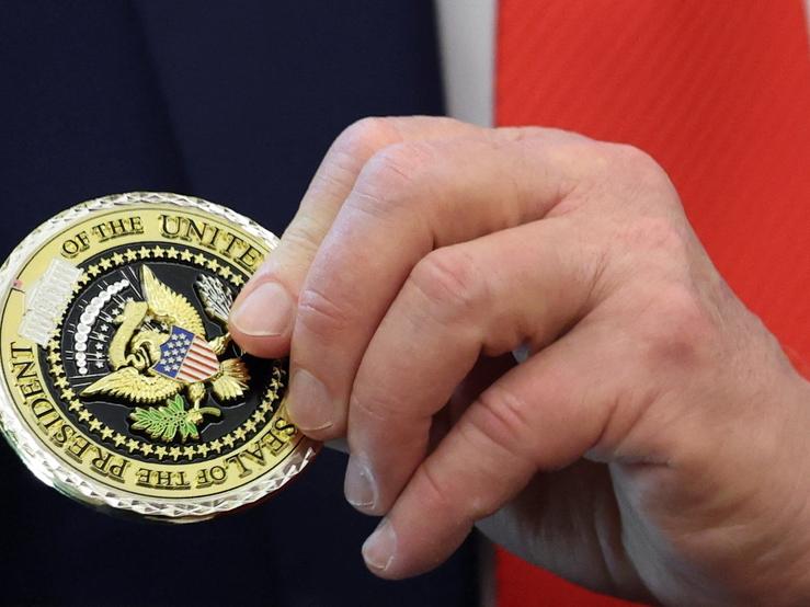 Trump’s hand holding a medal with the presidential seal