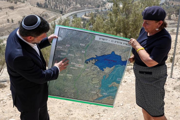 Israeli Finance Minister Bezalel Smotrich and a woman hold a map that shows a West Bank settlement plan.