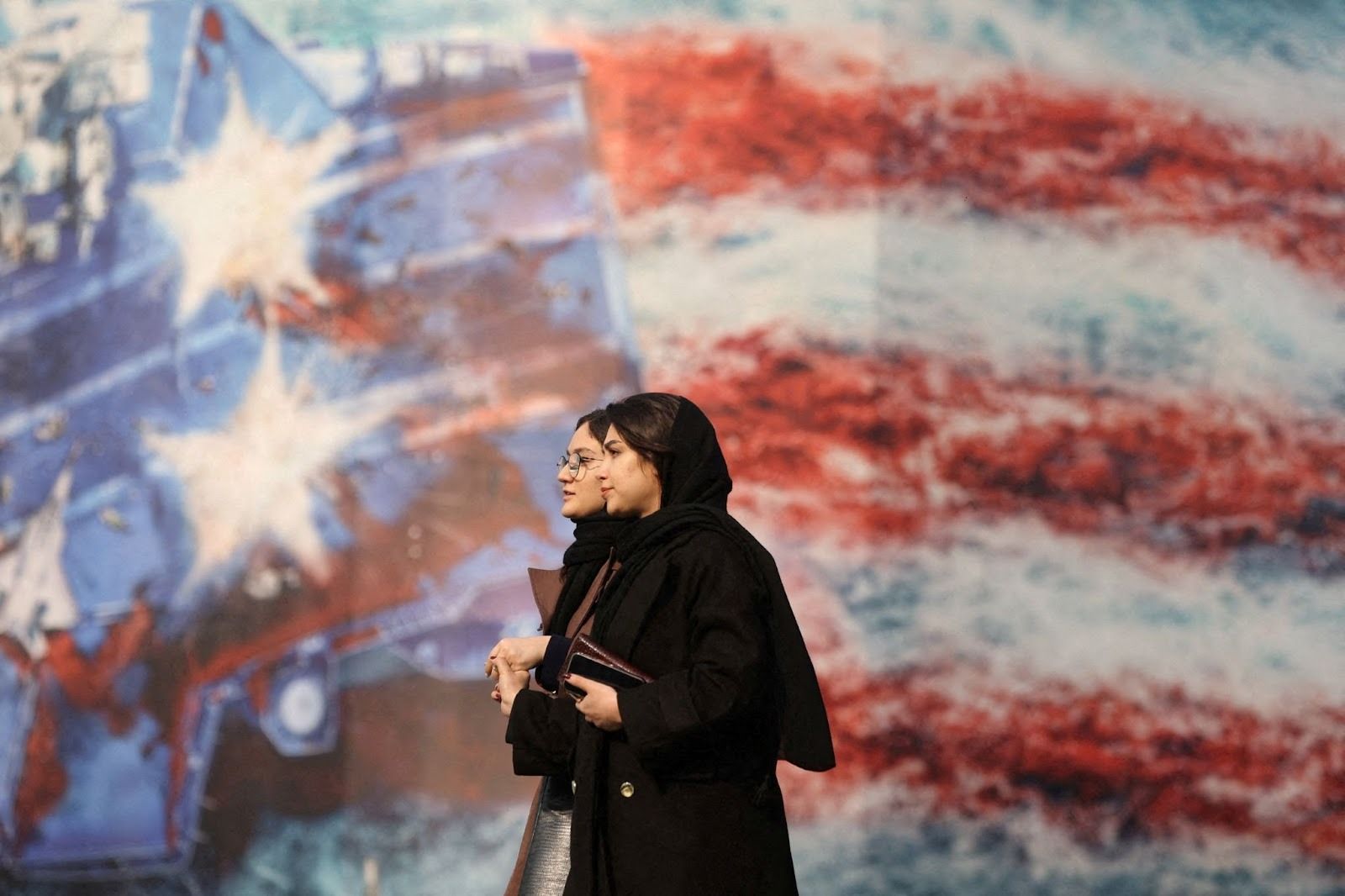 Two women in Iran walking in front of an anti-US billboard. 