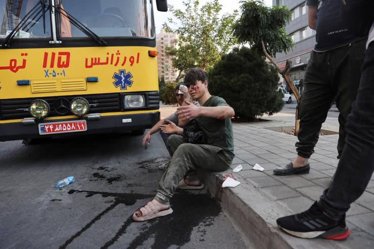 An injured person sits on a roadside in the aftermath of Israeli strikes, in Tehran, Iran.