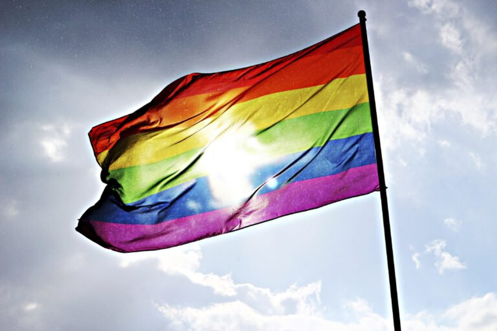 A image of a rainbow flag with the sun shining through.