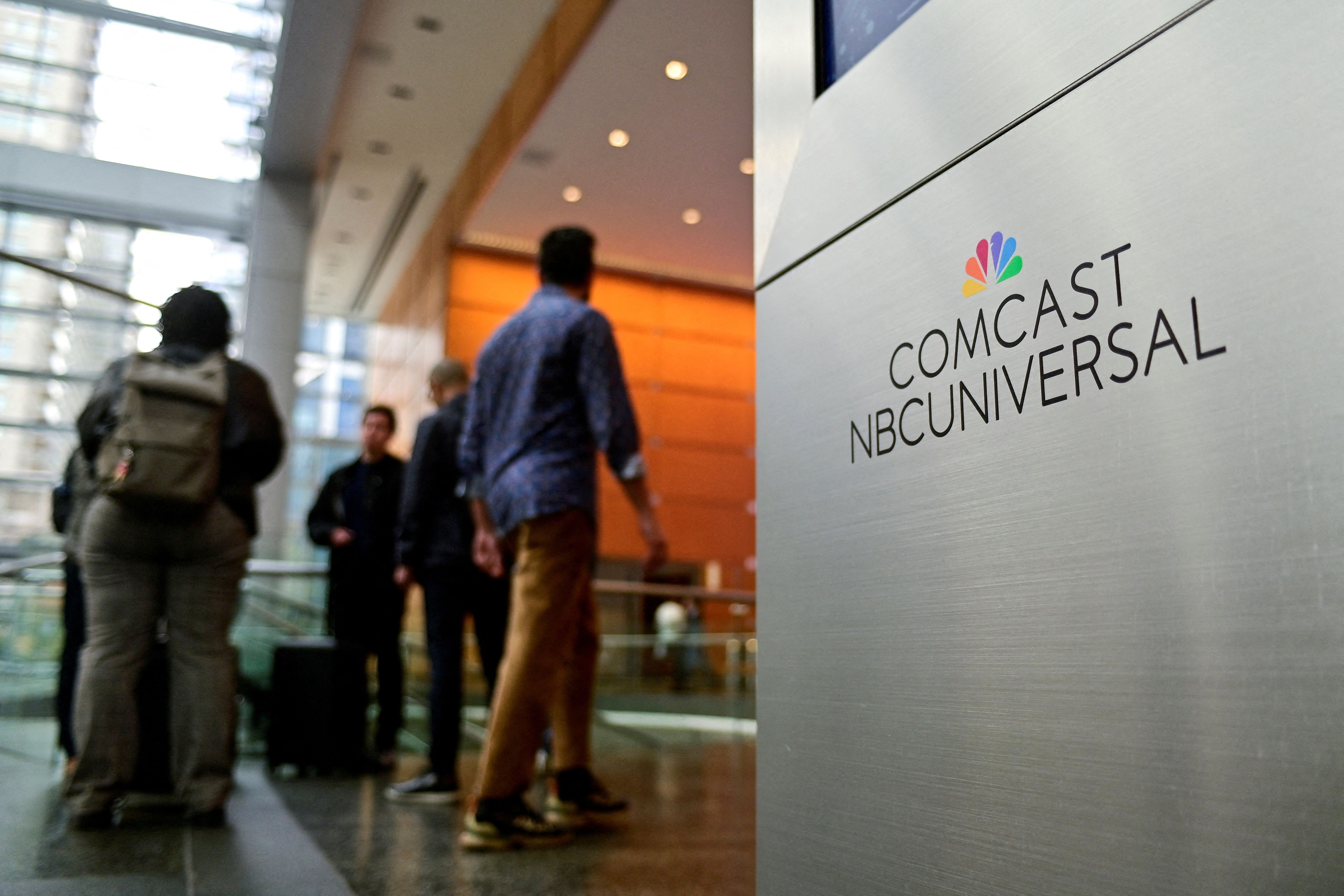 People stand near a signage of Comcast and NBC Universal in the lobby of the corporate headquarters of Comcast